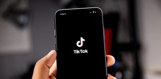 Hand med mobil med TikTok som endrar aldresgrense på strøyming.