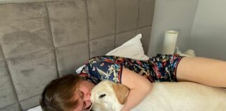 Lidia ligg på ei seng med ein labrador retriever.
