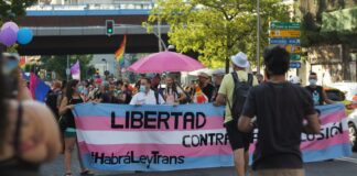 Tog med eit banner for ny translov i Spania, der det står "Libertad" og "#HabráLeyTrans" med fargane til transflagget.