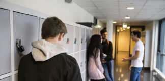 Elevar i ein korridor på skulen. Ein elev står aleine med tre andre står i ring og pratar saman.
