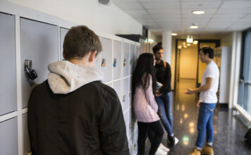 Elevar i ein korridor på skulen. Ein elev står aleine med tre andre står i ring og pratar saman.