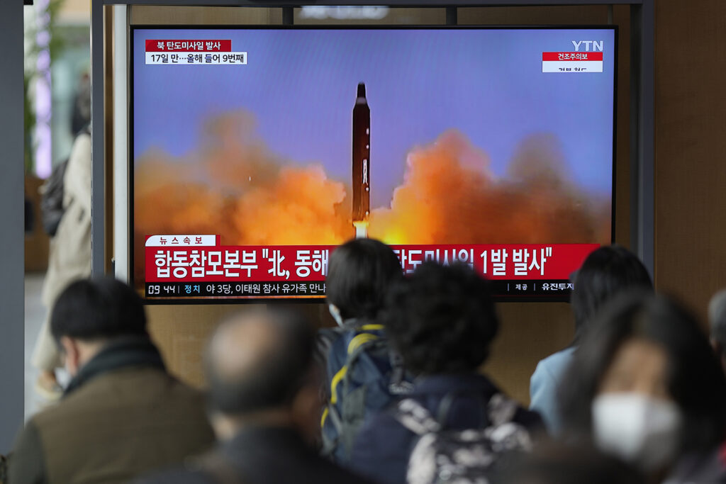TV-skjerm med koreansk tekst som viser oppskyting av rakett, med folk som står framfor.