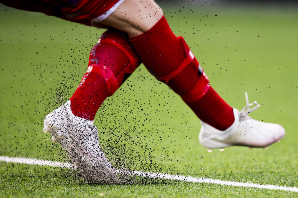 Ein fot sparkar opp masse gummigranulat på ei fotballbane.