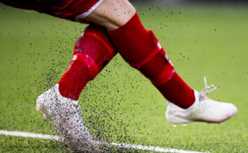 Ein fot sparkar opp masse gummigranulat på ei fotballbane.