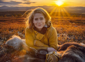Kvinne med blondt hår og friluftsklær ligger på en skinfell i solnedgang