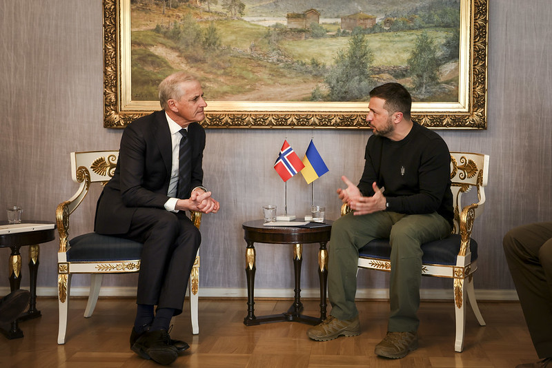 To menn sit på kvar sin stor, med eit lite bord med norsk og ukrainsk flagg.