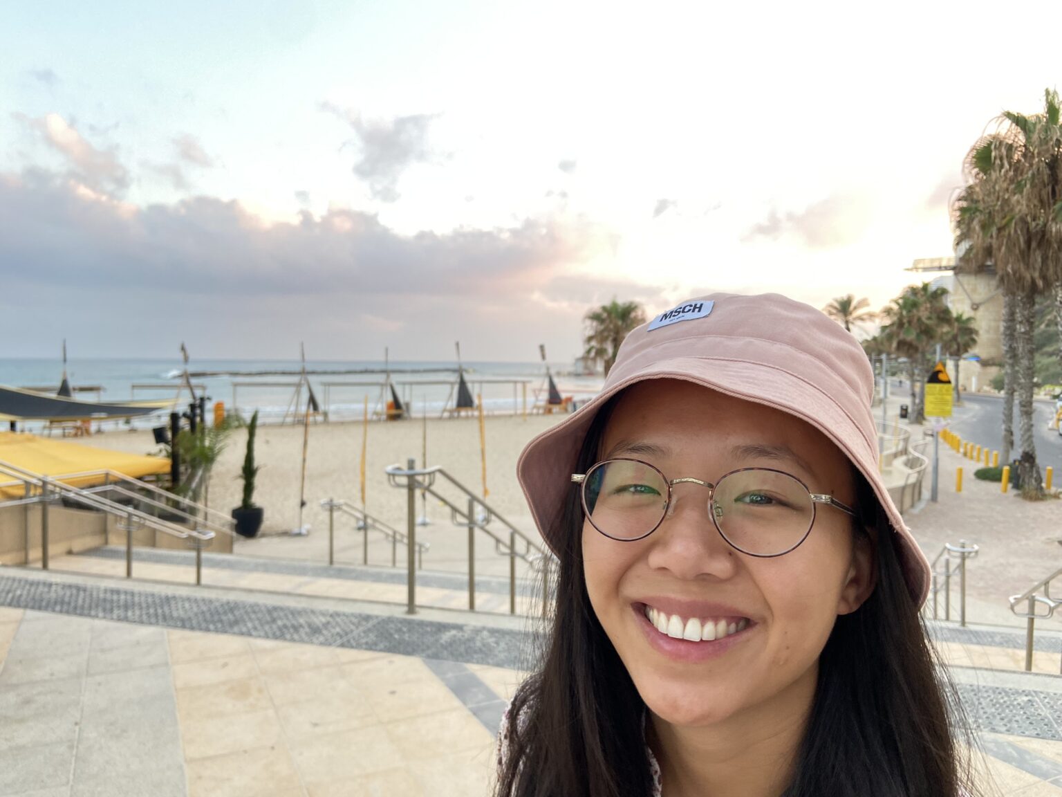 Kvinne med mørkt hår tek selfie framfor strand.