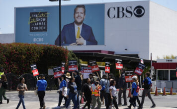 Ei folkemengde med skilt og ropert framfor eit billboard på ein bygning der det står CBS.