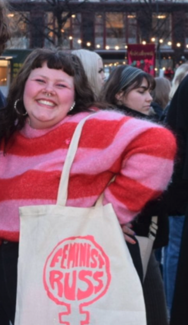 Ung kvinne i raud og rosa genser med berenett med logoen til Feministruss.