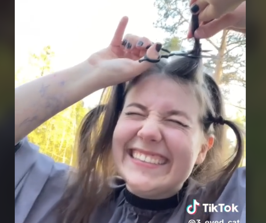 Kvinne med spent ansiktsutrykk klipper av ei musehalet på toppen av håret sitt.