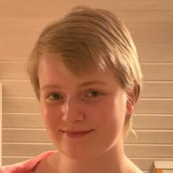 Kvinne med kort hår stripete topp og rosa jakke.