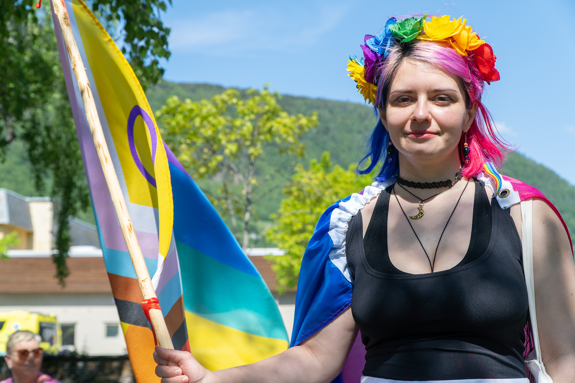 Kvinne med blomsterkrans i regnbogefarger på hovudet og Intersex Progress regnbogeflagget i handa.