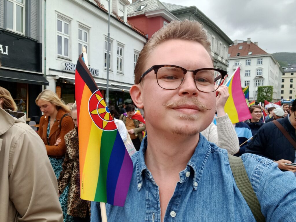 Ung mann med bart og briller held ein regnbogeversjon av det kvenske flagget.