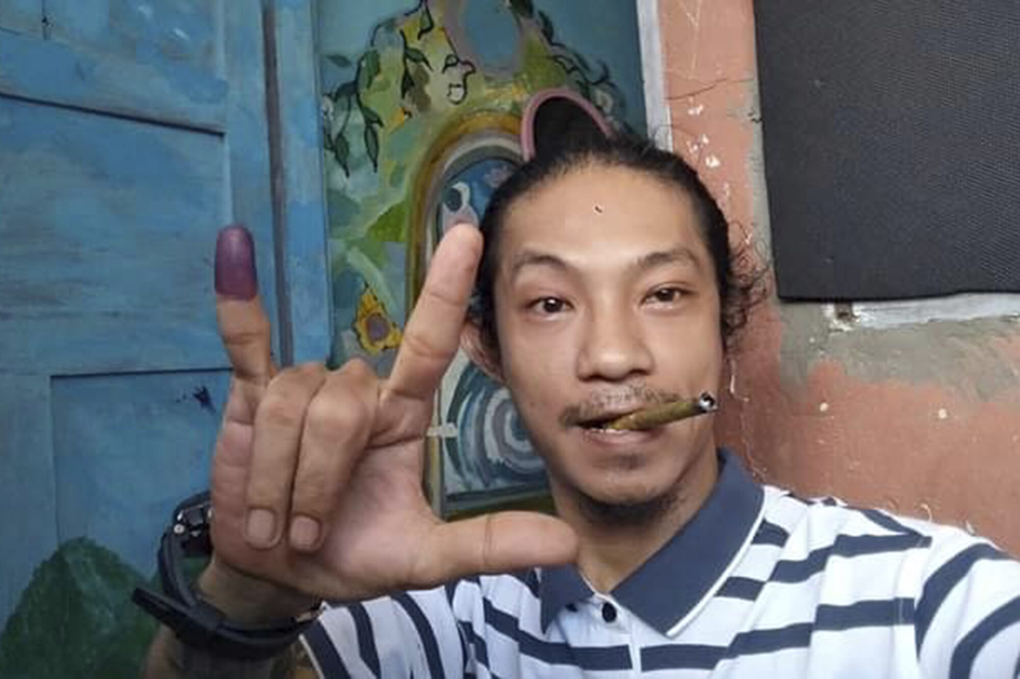 Mann med sigar i munnen viser teikn med fingrane i ein selfie.