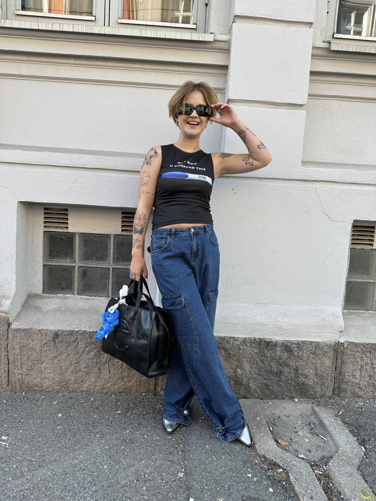 Ung kvinne poserer i jeans, singlet og solbriller.