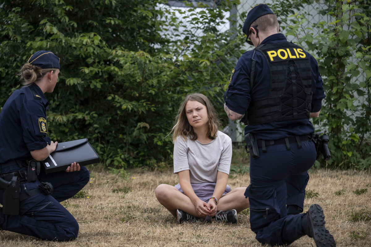Ung kvinne sit på bakken omringa av to politi. Dei gjer seg klare til å arrestera ho.