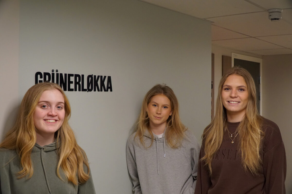 Tre jenter som smiler til kamera ved sidan av eit skilt kor det står "Grünerløkka".
