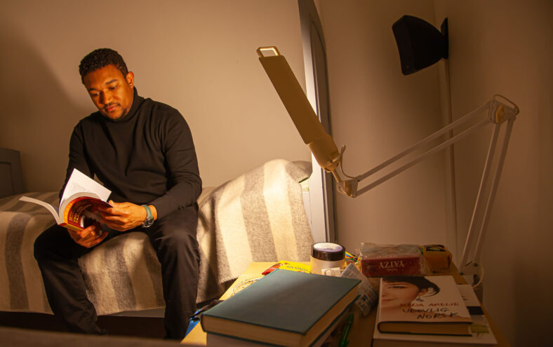 Melaninrik mann sitter på en seng og leser