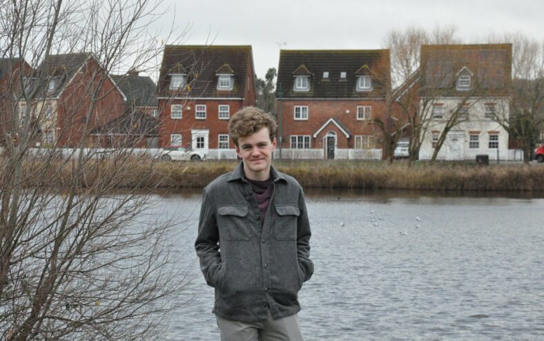 Sam Carling står foran ei elv i ein engelsk landsby