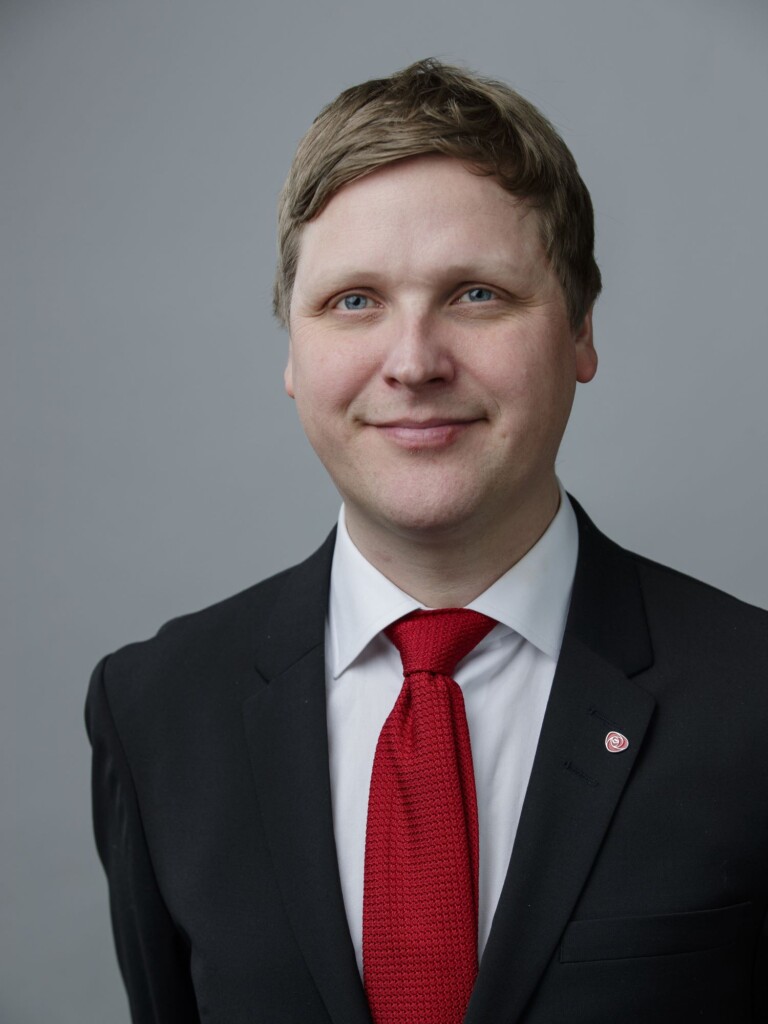 Mann med raudt slips ser i kameraet og smiler.